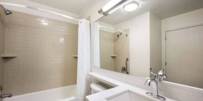 Guest bathroom in Sonesta Simply Suites Dallas Las Colinas, featuring bath with a shower, mirror, sink, and lavatory.