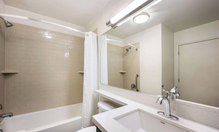 Guest bathroom in Sonesta Simply Suites Dallas Las Colinas, featuring bath with a shower, mirror, sink, and lavatory.