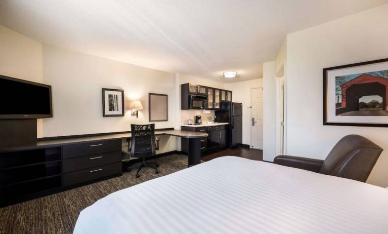 Sonesta Simply Suites Dallas Las Colinas double bed guest room, furnished with armchair, TV, and workspace desk and chair.