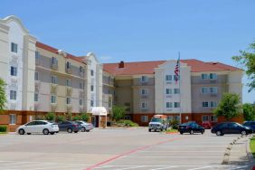 The hotel’s exterior has ample parking for guests, a US flag fluttering on a flagpole, and abundant greenery.