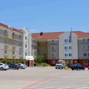 The hotel’s exterior has ample parking for guests, a US flag fluttering on a flagpole, and abundant greenery.