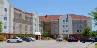 The hotel’s exterior has ample parking for guests, a US flag fluttering on a flagpole, and abundant greenery.