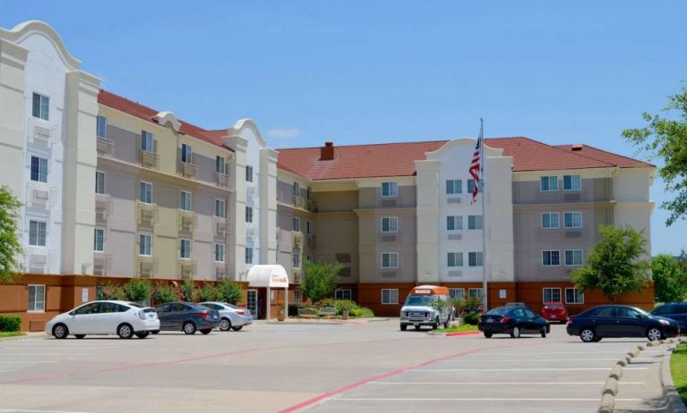 The hotel’s exterior has ample parking for guests, a US flag fluttering on a flagpole, and abundant greenery.