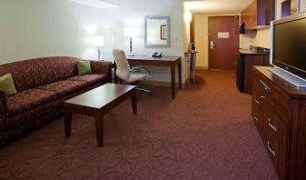 Sonesta Milwaukee West Wauwatosa guest room workspace with desk, chair, lamp, and telephone, with TV and sofa nearby.