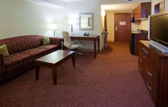 Sonesta Milwaukee West Wauwatosa guest room workspace with desk, chair, lamp, and telephone, with TV and sofa nearby.