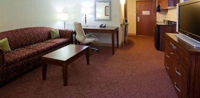 Sonesta Milwaukee West Wauwatosa guest room workspace with desk, chair, lamp, and telephone, with TV and sofa nearby.