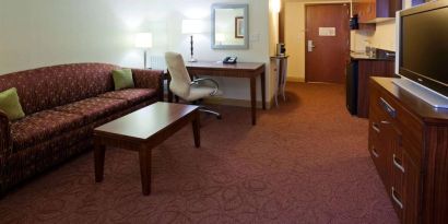 Sonesta Milwaukee West Wauwatosa guest room workspace with desk, chair, lamp, and telephone, with TV and sofa nearby.