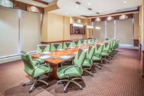 Hotel meeting room, furnished with a long wooden table and 18 green swivel chairs.