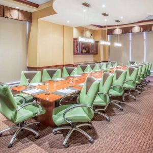 Hotel meeting room, furnished with a long wooden table and 18 green swivel chairs.