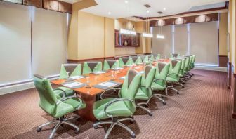 Hotel meeting room, furnished with a long wooden table and 18 green swivel chairs.