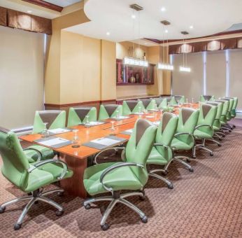 Hotel meeting room, furnished with a long wooden table and 18 green swivel chairs.