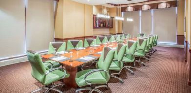 Hotel meeting room, furnished with a long wooden table and 18 green swivel chairs.