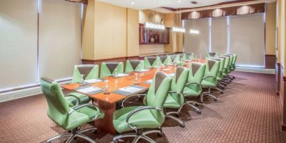 Hotel meeting room, furnished with a long wooden table and 18 green swivel chairs.