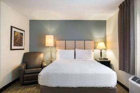 Sonesta Simply Suites Hampton double bed guest room, featuring window, art on the wall, and an armchair.