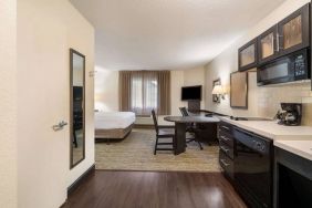 Sonesta Simply Suites Hampton double bed guest room, with kitchen, chairs, window, and a TV.