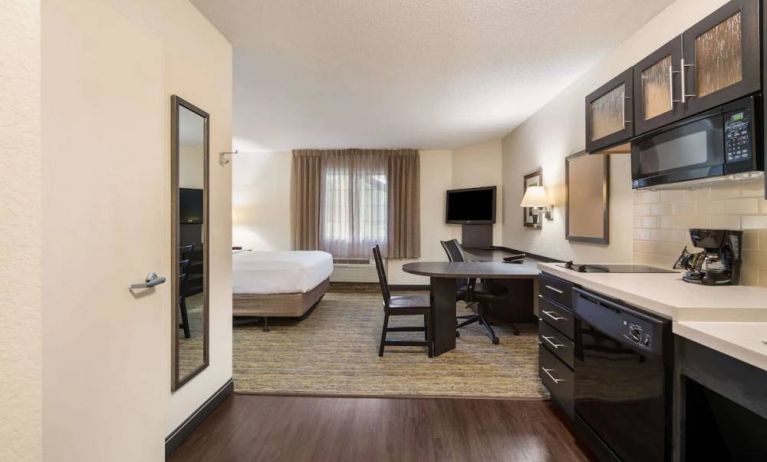 Sonesta Simply Suites Hampton double bed guest room, with kitchen, chairs, window, and a TV.