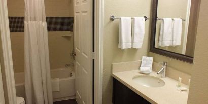 Guest bathroom in Sonesta ES Suites Dallas Las Colinas, featuring bath with a shower, lavatory, and mirror and sink.