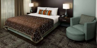 Double bed guest room in Sonesta ES Suites Dallas Las Colinas, featuring armchair, bedside lamps, and a window.