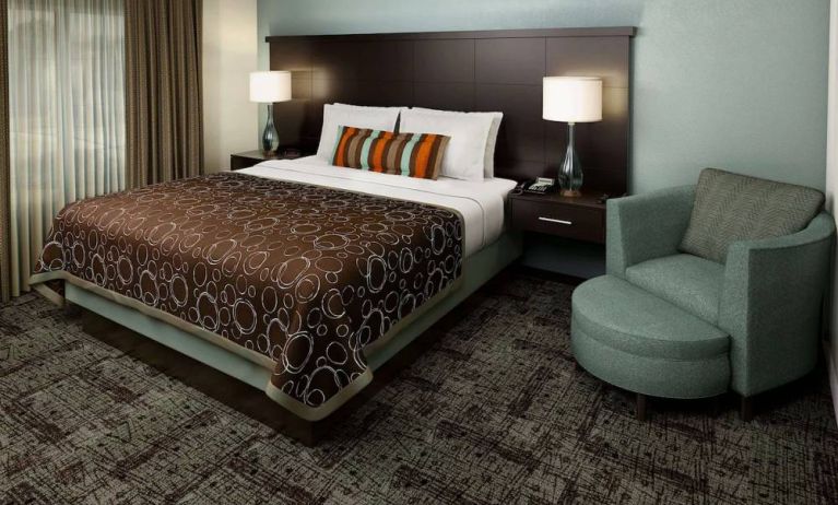 Double bed guest room in Sonesta ES Suites Dallas Las Colinas, featuring armchair, bedside lamps, and a window.