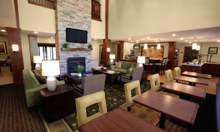 The hotel’s lounge is furnished with armchair and sofa seating around coffee tables, with a wall-mounted TV, and more tables and chairs nearby.