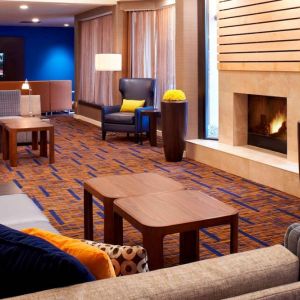 Sonesta Select Detroit Auburn Hills’ lobby lounge is furnished with sofas, armchairs, coffee tables, a fireplace and a wall-mounted TV.