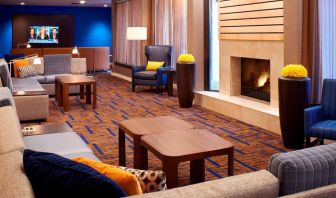 Sonesta Select Detroit Auburn Hills’ lobby lounge is furnished with sofas, armchairs, coffee tables, a fireplace and a wall-mounted TV.