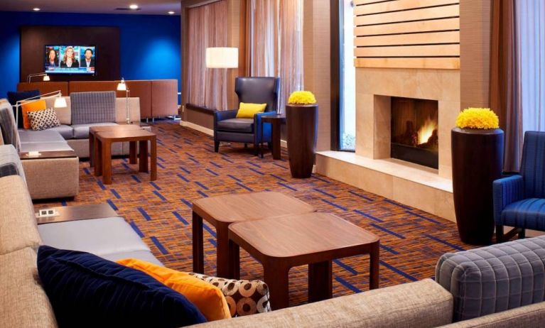 Sonesta Select Detroit Auburn Hills’ lobby lounge is furnished with sofas, armchairs, coffee tables, a fireplace and a wall-mounted TV.