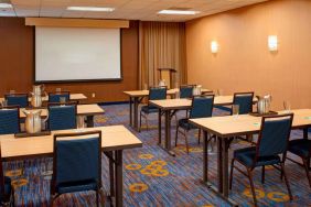 Hotel meeting room with seating for a dozen attendees and tables arranged in a classroom format facing a projector screen.