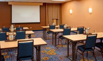 Hotel meeting room with seating for a dozen attendees and tables arranged in a classroom format facing a projector screen.