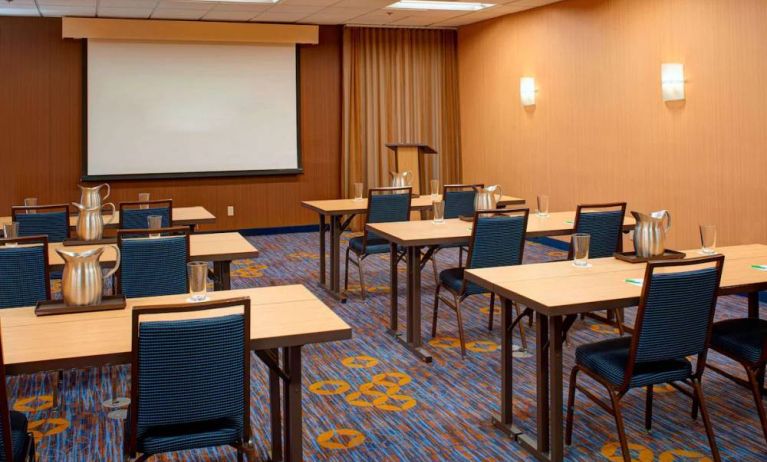 Hotel meeting room with seating for a dozen attendees and tables arranged in a classroom format facing a projector screen.