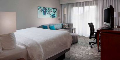 Sonesta Select Boca Raton double bed guest room, including sofa, window, TV, and a workspace desk and chair.