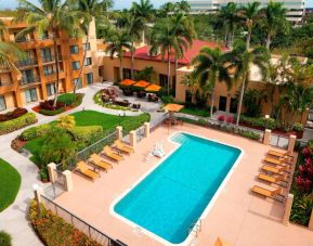 Sonesta Select Boca Raton’s outdoor pool is equipped with a lift, and has sun loungers by the side plus pleasant greenery beyond the fence.