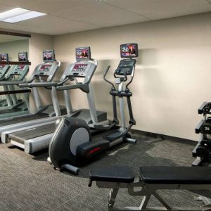 The fitness center at Sonesta Select Boca Raton comes with a wall-mounted TV, a variety of exercise machines, and rows of free weights.