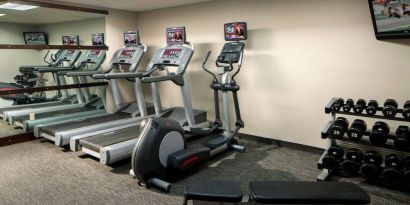 The fitness center at Sonesta Select Boca Raton comes with a wall-mounted TV, a variety of exercise machines, and rows of free weights.