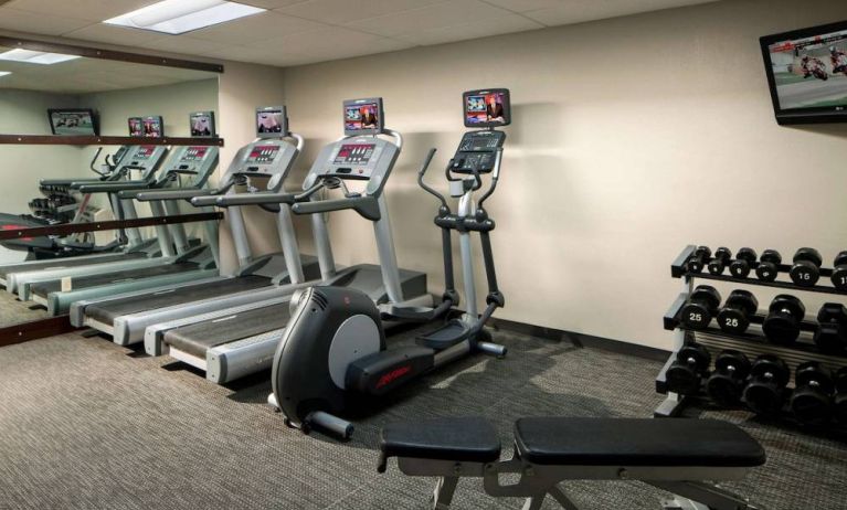 The fitness center at Sonesta Select Boca Raton comes with a wall-mounted TV, a variety of exercise machines, and rows of free weights.