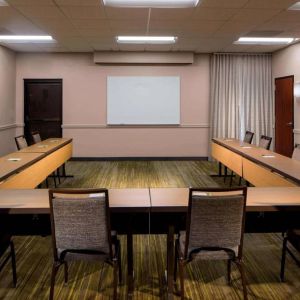 Hotel meeting room, featuring tables arranged in a U-shape, seating for a dozen attendees, and a whiteboard.