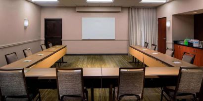 Hotel meeting room, featuring tables arranged in a U-shape, seating for a dozen attendees, and a whiteboard.