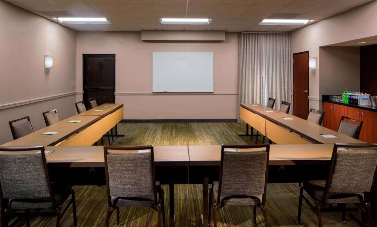 Hotel meeting room, featuring tables arranged in a U-shape, seating for a dozen attendees, and a whiteboard.