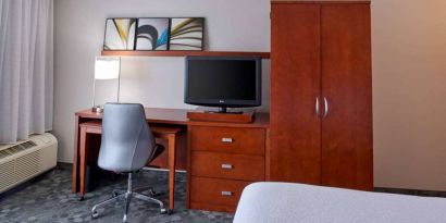 Sonesta Select Indianapolis Carmel guest room workspace, furnished with bed and TV, plus desk, chair, and lamp.