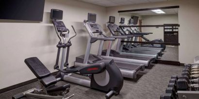 The hotel fitness center is equipped with free weights, a range of exercise machines, and a wall-mounted TV.