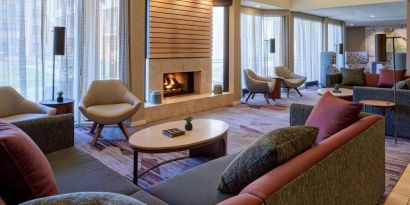 The lobby lounge in Sonesta Select Indianapolis Carmel has a mix of comfy chairs and large sofas, plus coffee tables and a fireplace.