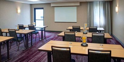 Hotel meeting room with tables, in a classroom format, facing a whiteboard and window.