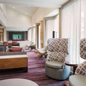 The lobby lounge at Sonesta Select Whippany Hanover features sofas and armchairs, coffee tables, large windows, and a large TV.