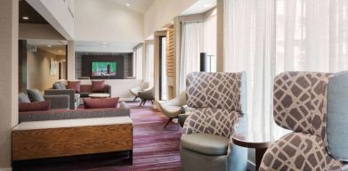 The lobby lounge at Sonesta Select Whippany Hanover features sofas and armchairs, coffee tables, large windows, and a large TV.