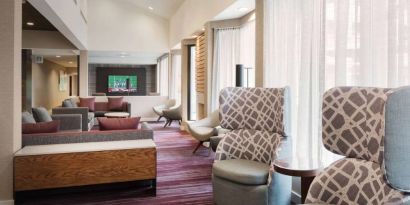 The lobby lounge at Sonesta Select Whippany Hanover features sofas and armchairs, coffee tables, large windows, and a large TV.