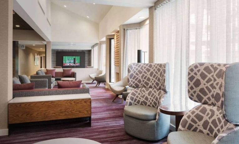 The lobby lounge at Sonesta Select Whippany Hanover features sofas and armchairs, coffee tables, large windows, and a large TV.