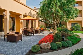 The hotel’s patio is furnished with a mix of tables and chairs, and sofa/armchair seating, next to flowerbeds and trees.