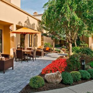 The hotel’s patio is furnished with a mix of tables and chairs, and sofa/armchair seating, next to flowerbeds and trees.