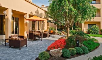 The hotel’s patio is furnished with a mix of tables and chairs, and sofa/armchair seating, next to flowerbeds and trees.