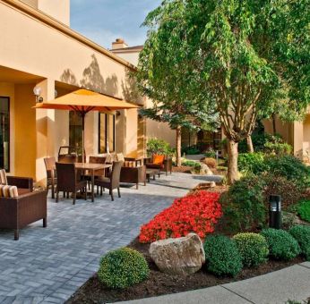 The hotel’s patio is furnished with a mix of tables and chairs, and sofa/armchair seating, next to flowerbeds and trees.